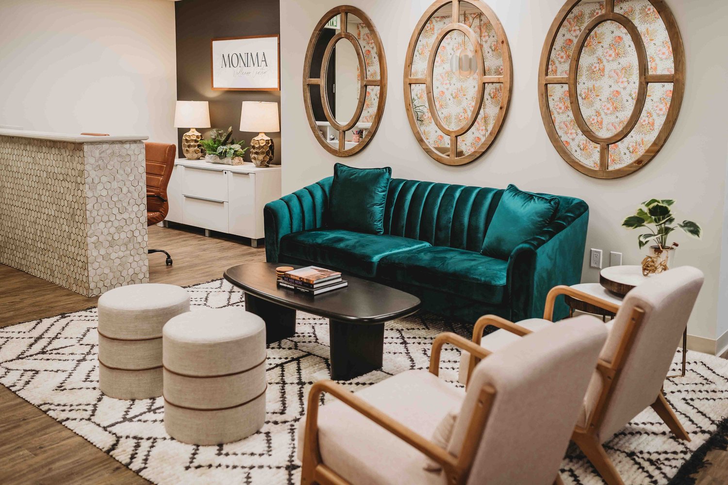 monima lounge: velvet green loveseat, two chairs, and two circle ottomans positioned around a black oval table with a stack of books. The reception table is on the left side