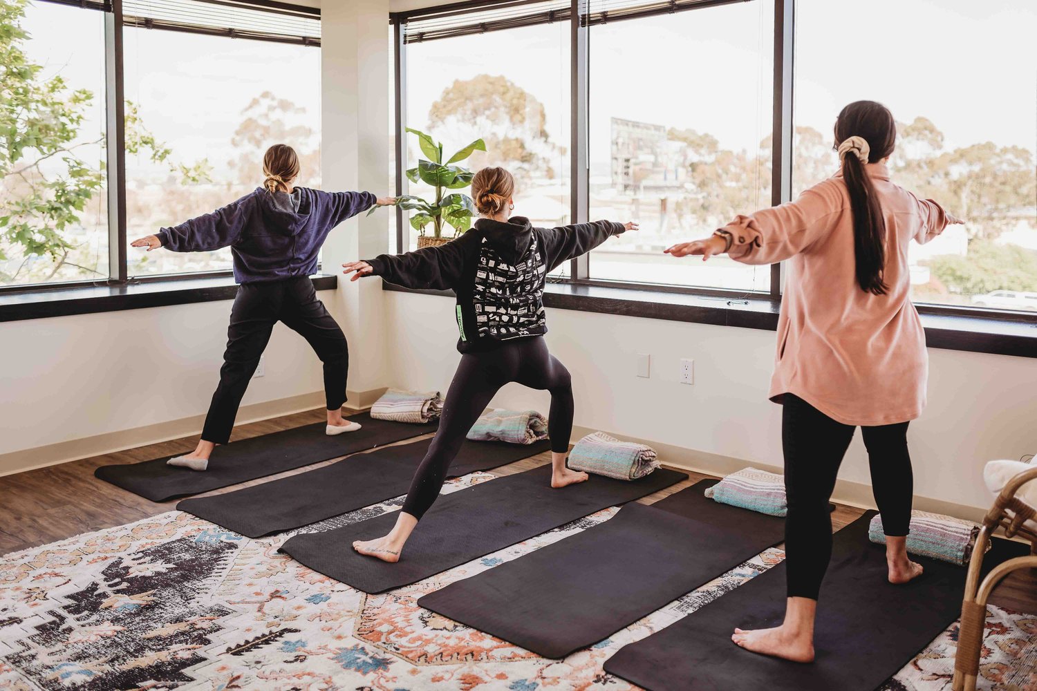 Yoga: three women practicing yoga on black yoga mats in front of a large window