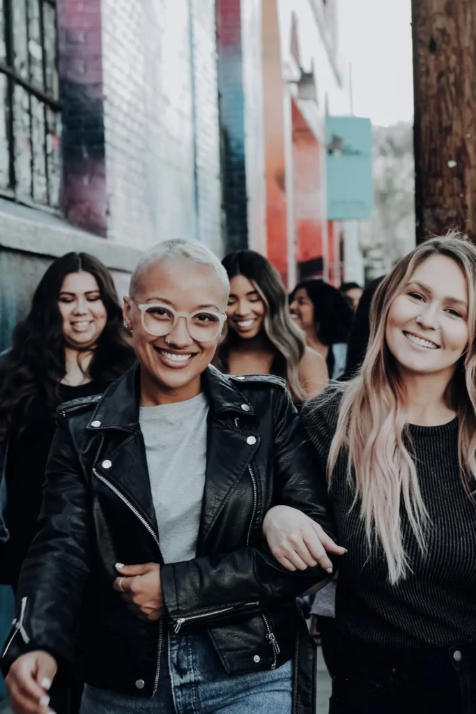 Group of women having an outing in town, walking down the street. Two women in front pose and smile at the camera