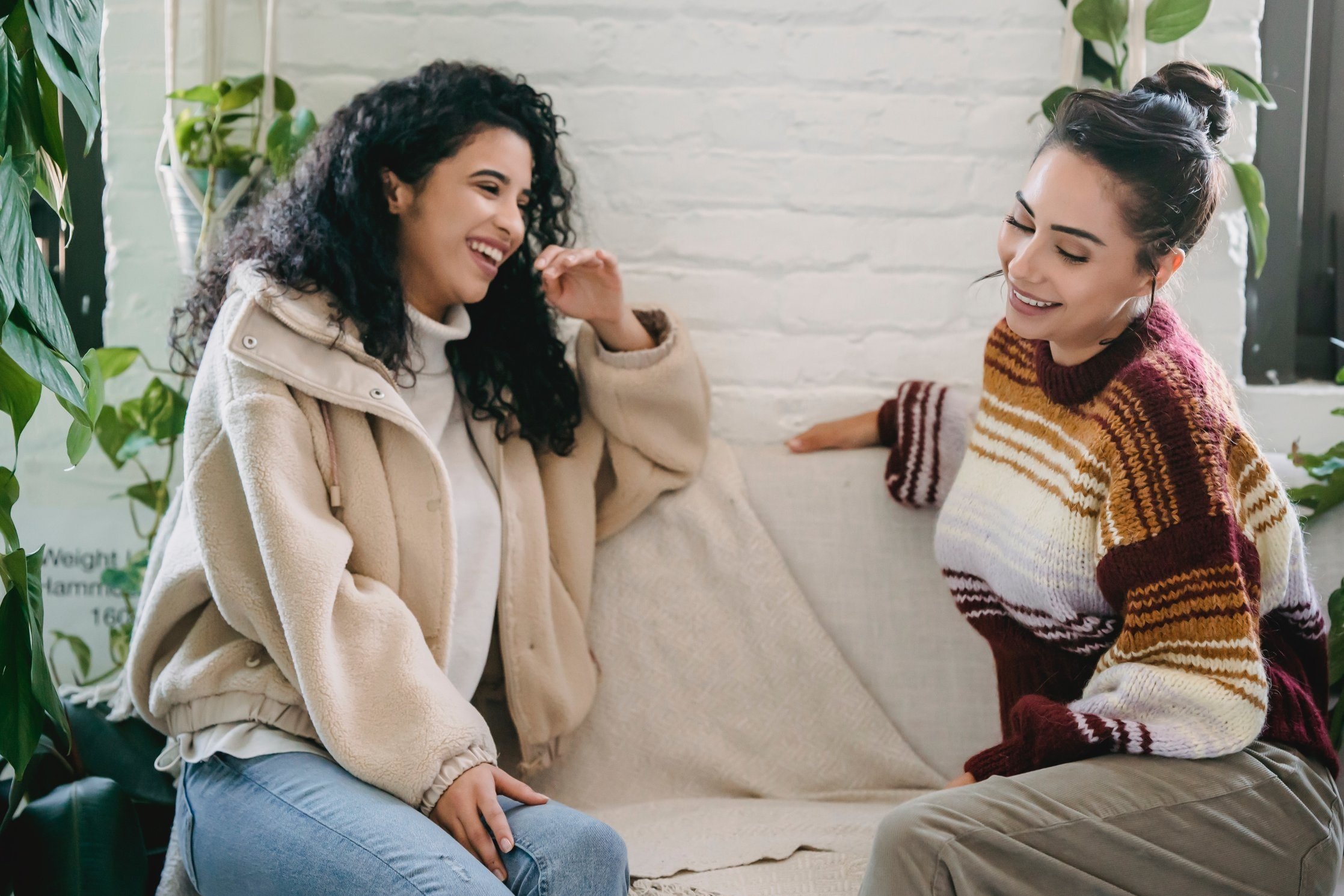 Two women sit on a couch having a lively conversation and smiling.