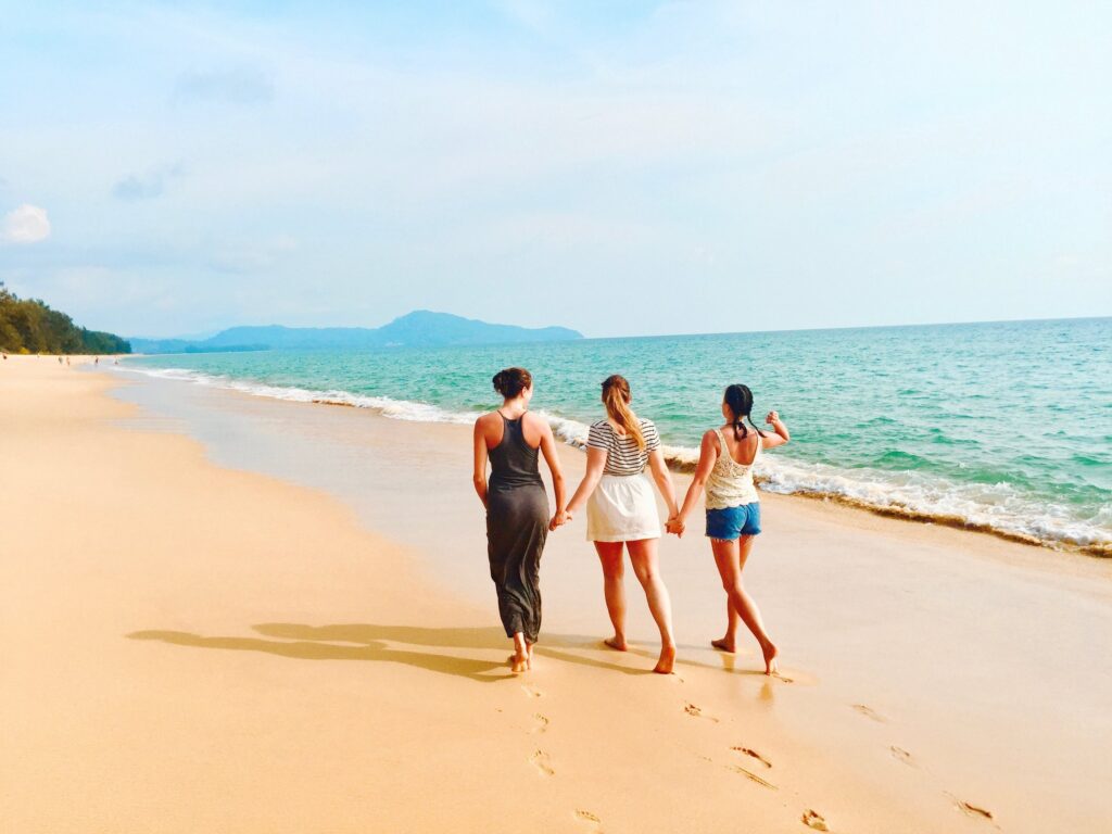 Three women holding hands and walking on the beach on a sunny day