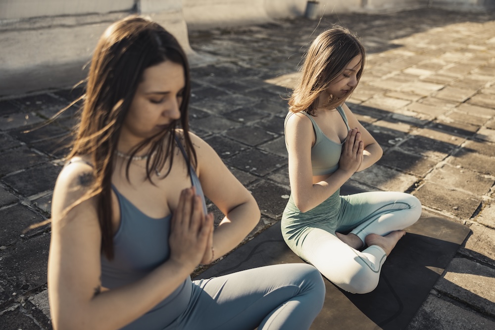Two young woman practicing yoga on a rooftop terrace.
