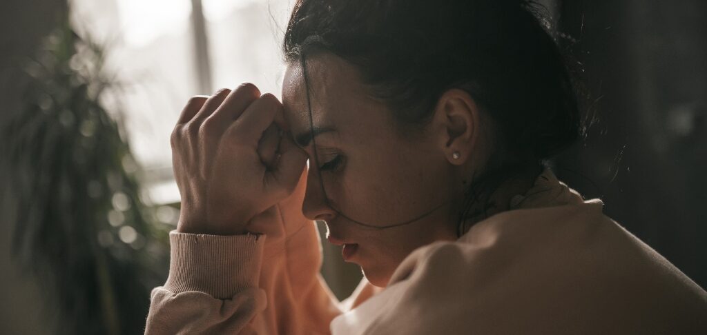 Young brunette woman with her head in her hands, struggling with emotional manipulation.