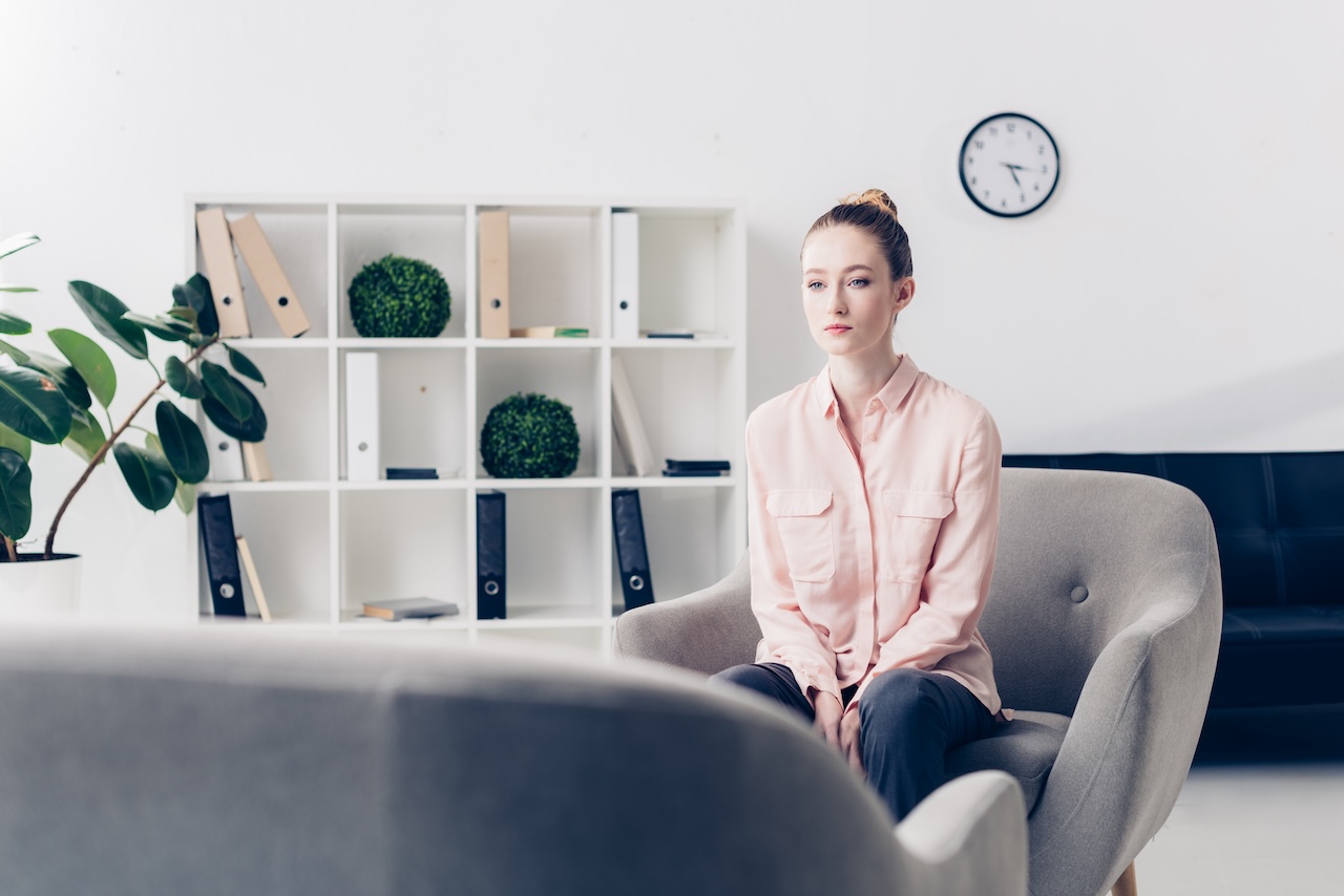 Young woman struggling internal battle, sitting in therapy office with plants, struggling with complex trauma.
