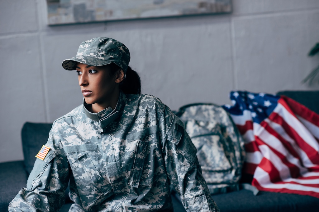 somber female soldier in military uniform with american flag on background