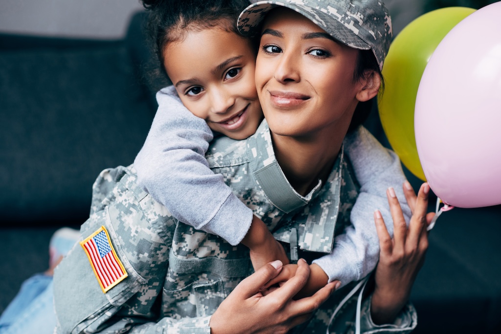 daughter hugging her mother in military uniform with balloons at home