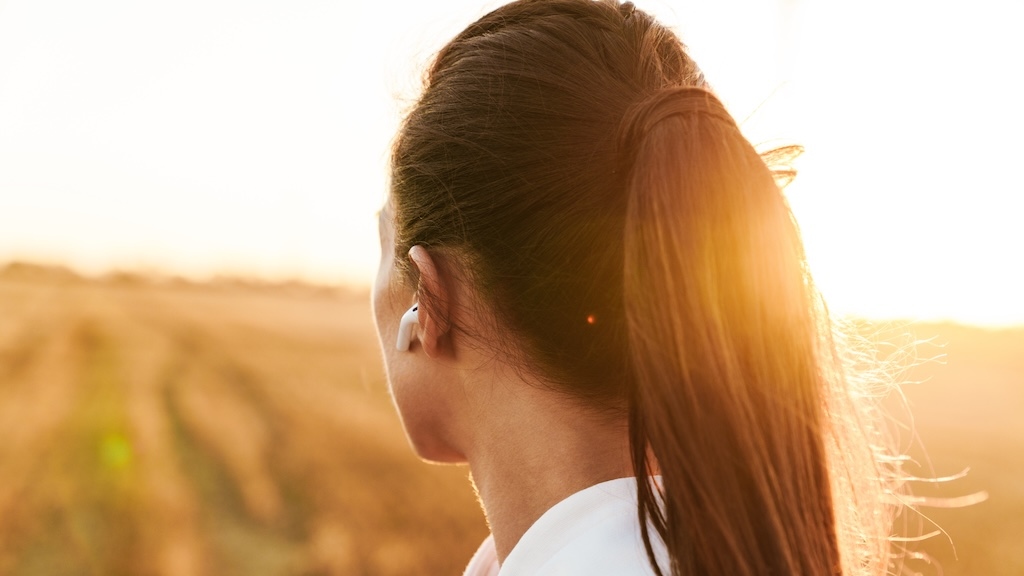Image of adult brunette sportswoman using earphones while working out at golden field