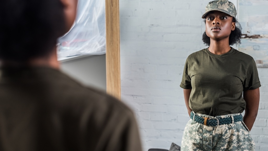 Young woman in camouflage clothes posing by the mirror