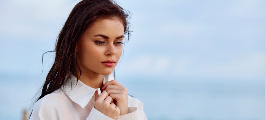 Portrait of a pensive woman with tanned skin in a white beach shirt