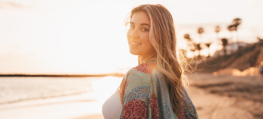 Portrait of one young beautiful woman on the sand of the beach enjoying and relaxing at the sunset of the day. Looking at the camera.