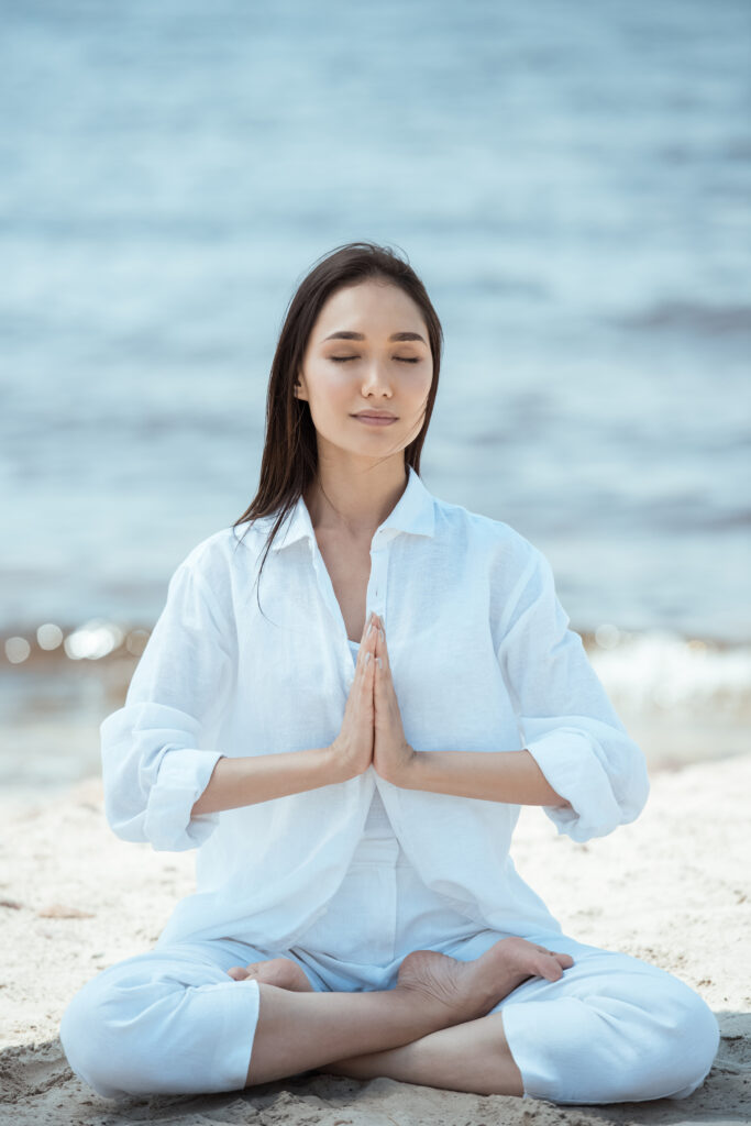 young woman in anjali mudra (salutation seal) pose on beach