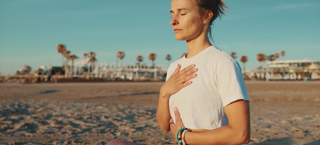 Beautiful woman keeping eyes closed sitting in lotus pose and meditating by the sea.