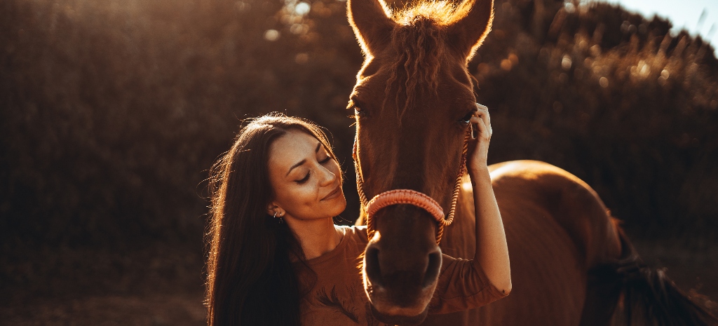 Woman with long dark hair at sunset hugging her horse