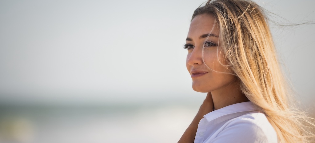 A tanned slender girl in a bluish swimsuit and a white light shirt, enjoys a warm sunny summer on the coast of a raging blue sea