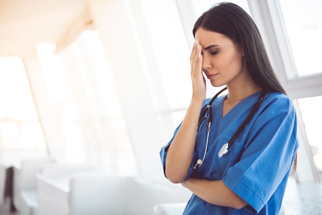 Beautiful doctor in blue scrubs is covering her face while standing in hospital corridor