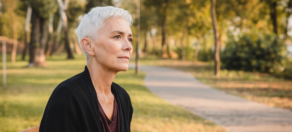 A thoughtful and reflective senior woman takes pleasure in a serene moment within a picturesque autumn park, where she is surrounded by an array of vibrant, colorful leaves that enhance the scene 