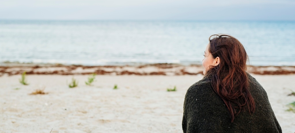 Rear view of woman wrapped in blanket sitting on beach
