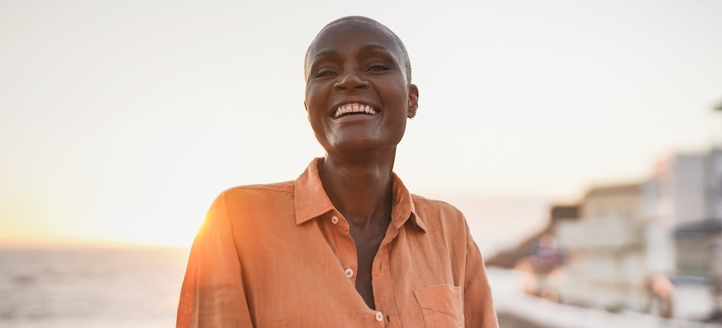 Happy senior african woman looking in camera - Beach and sunset in background