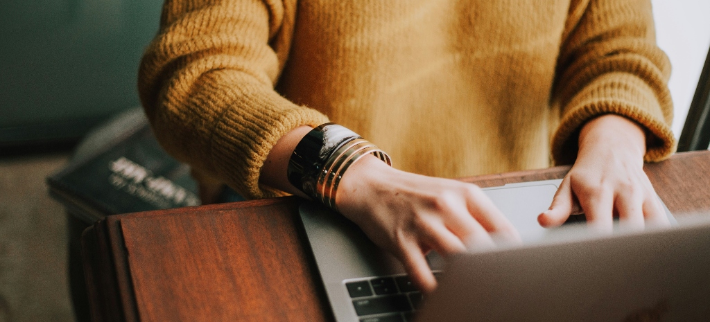 Woman searching treatment options on her laptop wearing dark yellow sweater. 