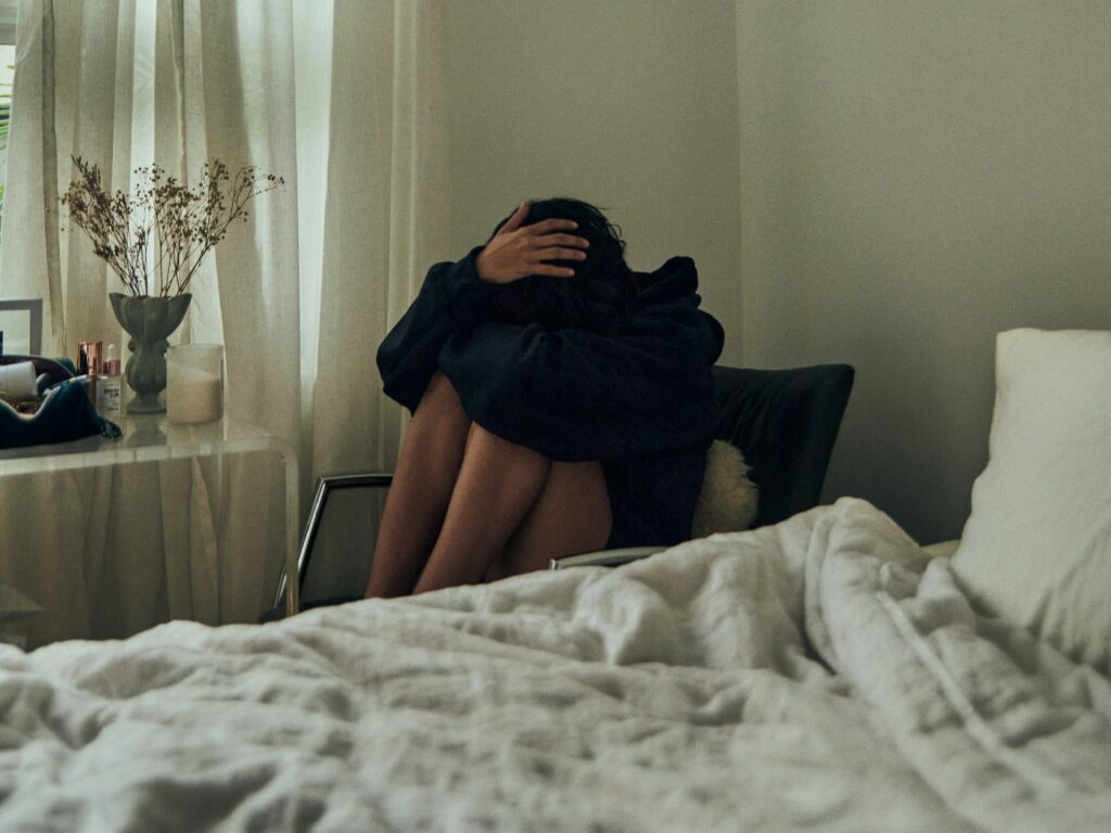 Young woman sitting in her bedroom with her head in her hands, wondering if she should seek treatment.