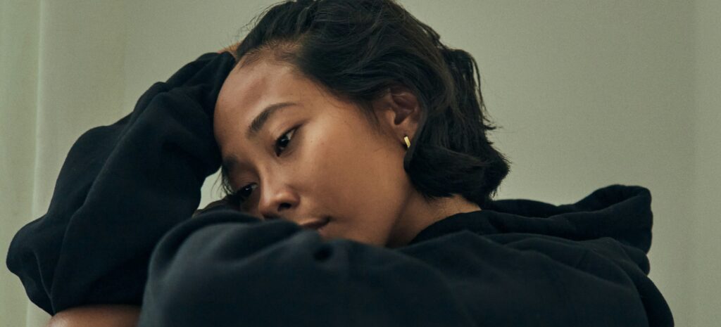 Young person with dark hair looking down at the ground. Displaying sadness, mental health struggles