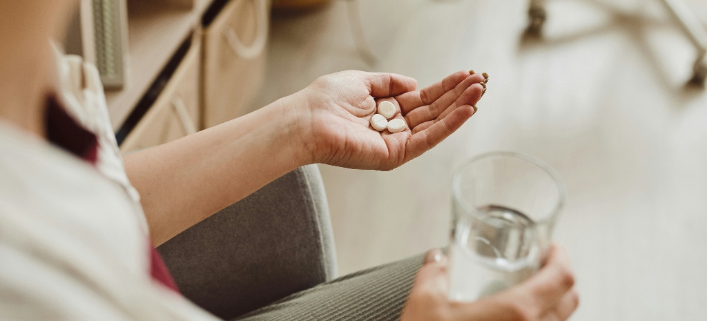 Woman holding pills in her hand with a glass of water