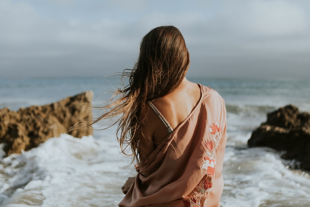 Woman standing at the shoreline looking out over the ocean, representing the beginning of a healing journey and taking the first step toward support and care