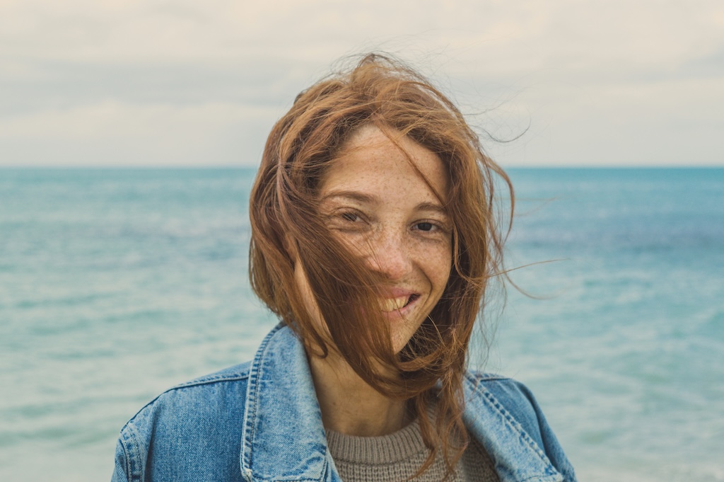 Woman by the ocean smiling in the breeze, representing healing and emotional recovery in trauma-focused treatment in San Diego