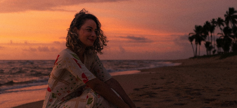 Woman sitting on the beach at sunset with a calm, reflective expression, representing emotional shifts and support for PMDD-related depression