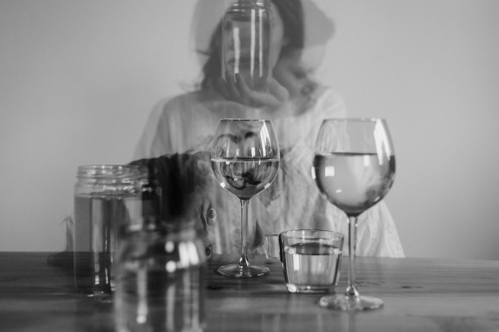 Woman reaching toward a glass of alcohol on a table with multiple drinks, reflecting disorientation and risk associated with alcohol poisoning in a women’s treatment context