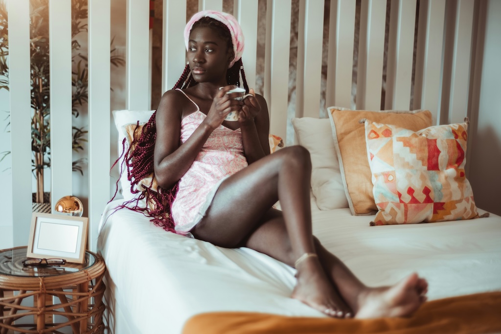 Woman sitting on bed holding a mug, looking thoughtful—representing premenstrual mood changes and PMDD.