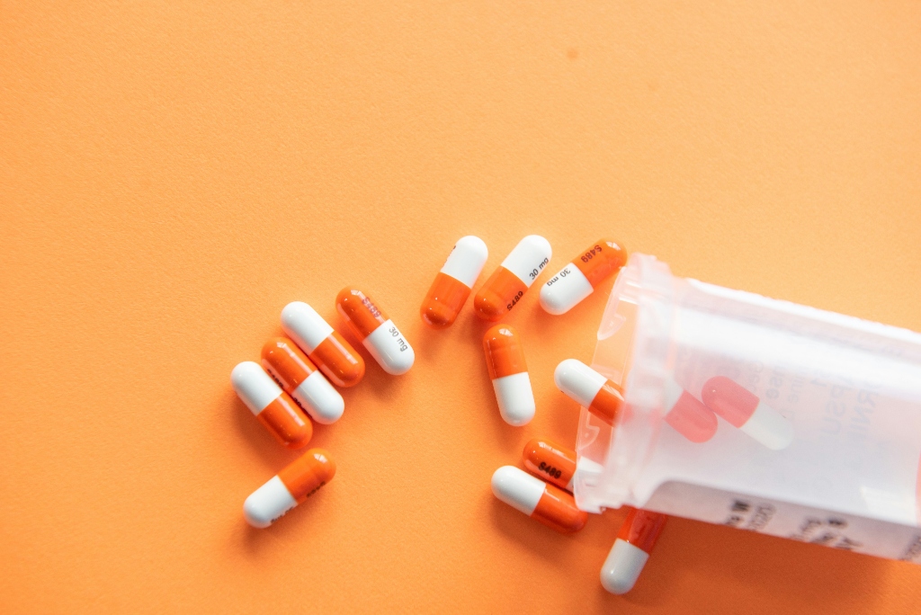 Orange and white Adderall capsules spilled from a prescription bottle, representing stimulant medication misuse and addiction concerns.
