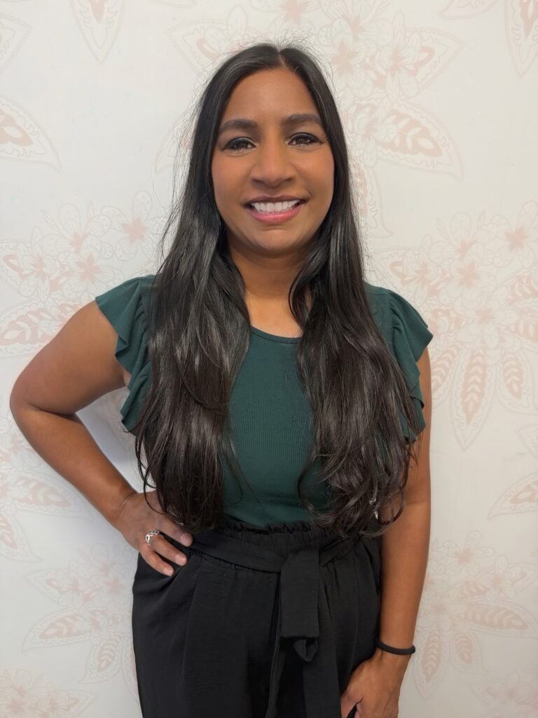 Dr. Lonika Misra, Doctor of Acupuncture and Chinese Medicine, smiling in a professional portrait wearing a green blouse and black pants.