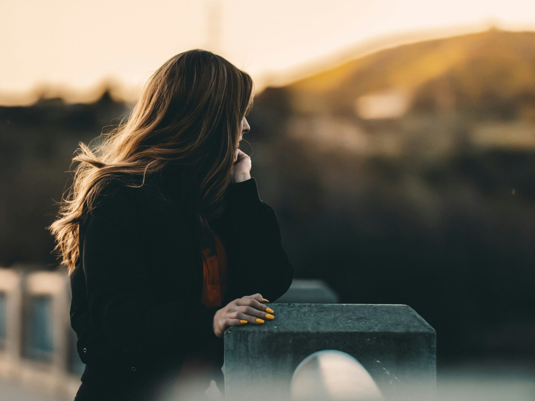 Woman standing outdoors and looking thoughtfully toward the sunset.