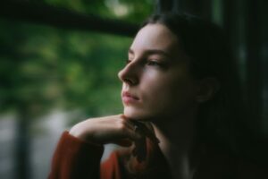 Woman looking thoughtfully out a window, representing the emotional and physical effects of alcohol withdrawal symptoms.