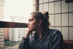 Woman looking out a window with a thoughtful expression, representing rejection sensitive dysphoria.