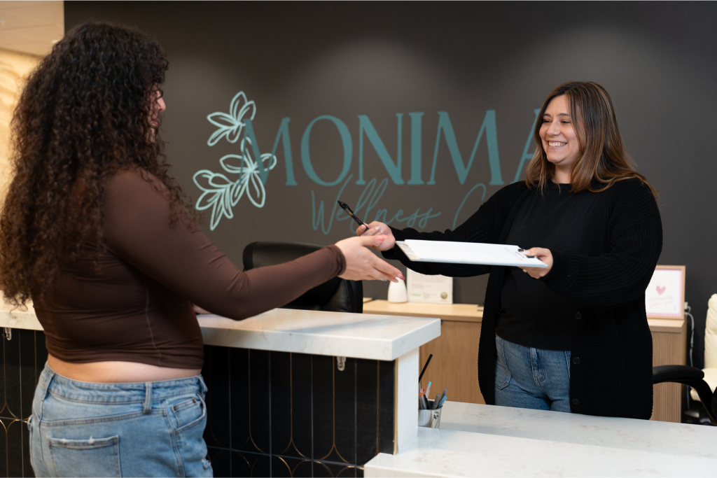 Monima Wellness staff member welcoming a woman at the front desk and handing her paperwork at the treatment center in San Diego.