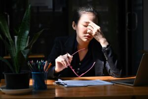 Woman sitting at a desk with her hand on her forehead, appearing stressed and overwhelmed while working, illustrating high-strung behavior.